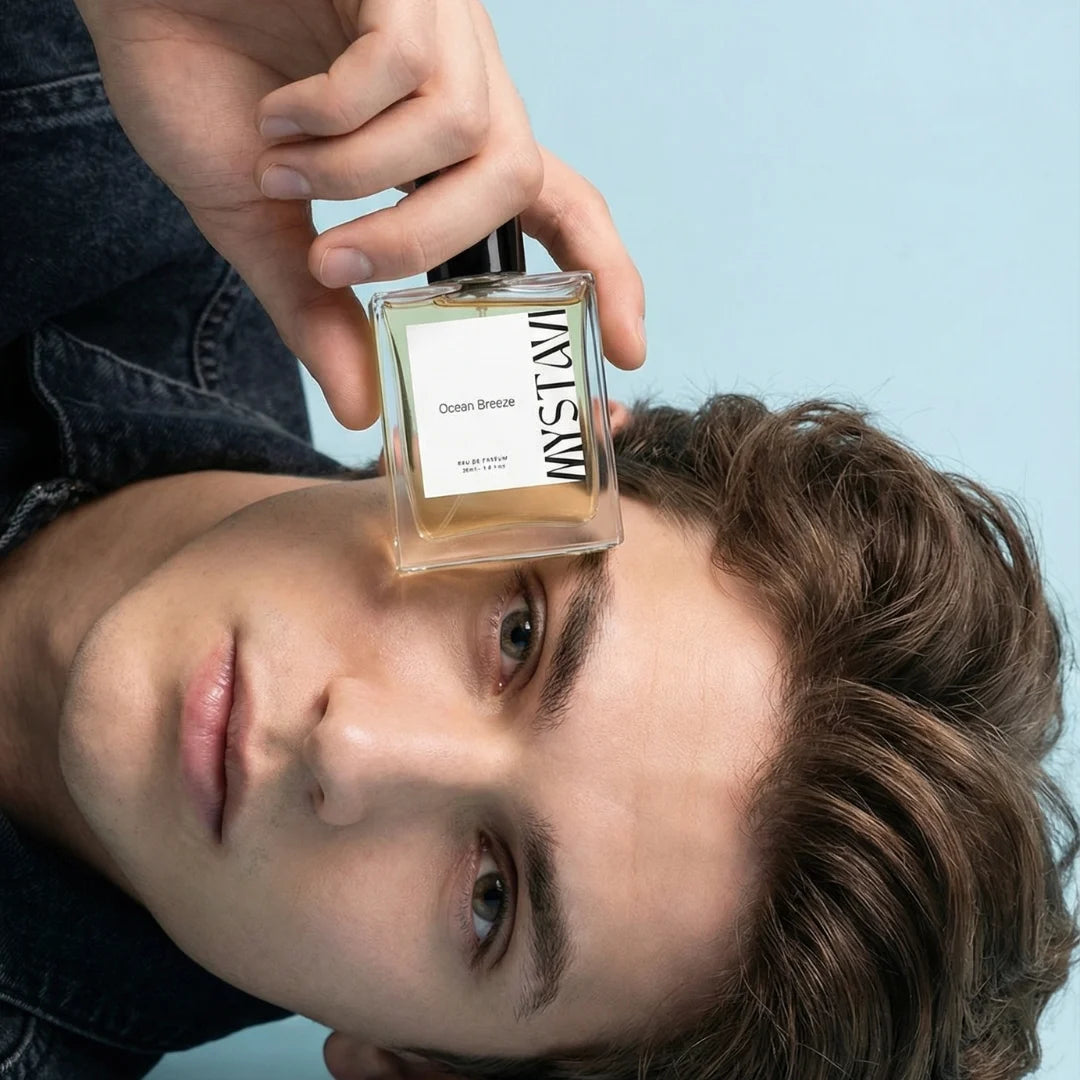 Person holding a perfume bottle labeled 'Mystavi' with a blue background